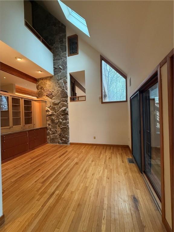 unfurnished living room featuring light wood-type flooring, a skylight, and high vaulted ceiling