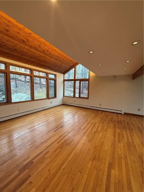 unfurnished living room featuring light hardwood / wood-style flooring, lofted ceiling with beams, and a baseboard heating unit