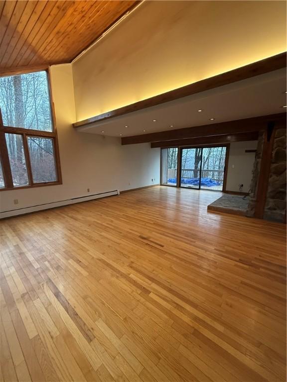 unfurnished living room featuring baseboard heating, a wealth of natural light, wood ceiling, and light hardwood / wood-style floors