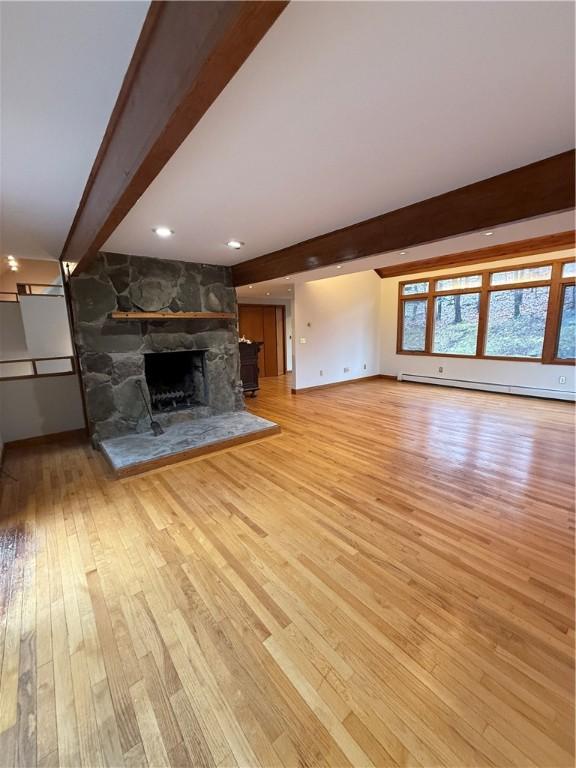 unfurnished living room featuring light hardwood / wood-style floors, a stone fireplace, beam ceiling, and a baseboard radiator