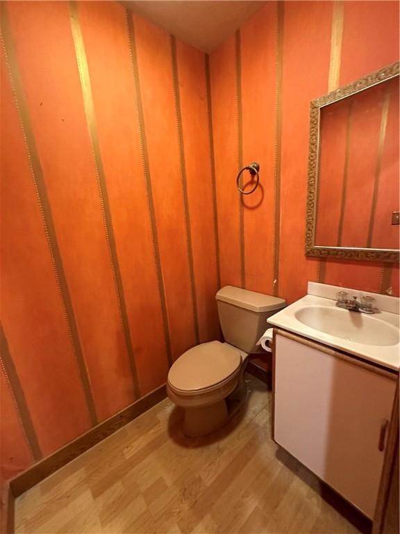 bathroom with wood walls, vanity, wood-type flooring, and toilet