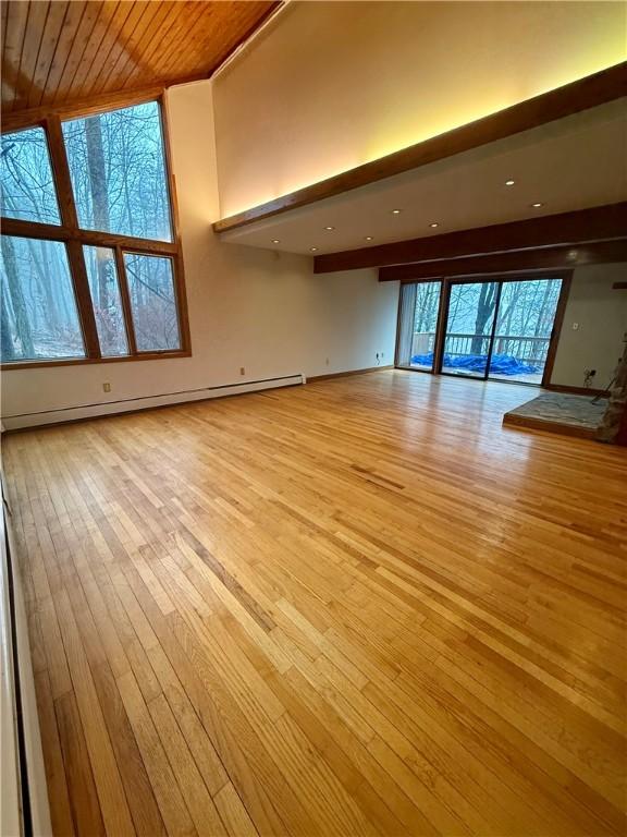 unfurnished living room featuring baseboard heating, wooden ceiling, light hardwood / wood-style flooring, and a healthy amount of sunlight