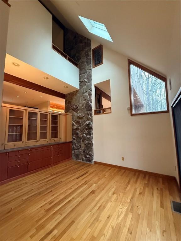 unfurnished living room featuring a skylight, a towering ceiling, and light hardwood / wood-style floors