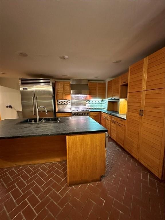 kitchen featuring kitchen peninsula, sink, stainless steel appliances, and wall chimney range hood