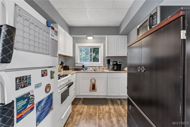 kitchen featuring hardwood / wood-style floors, a drop ceiling, pendant lighting, sink, and white cabinetry