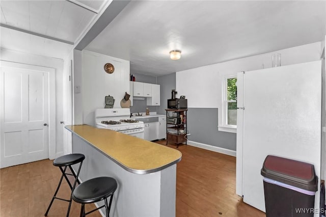 kitchen with white cabinetry, kitchen peninsula, hardwood / wood-style floors, white appliances, and a breakfast bar