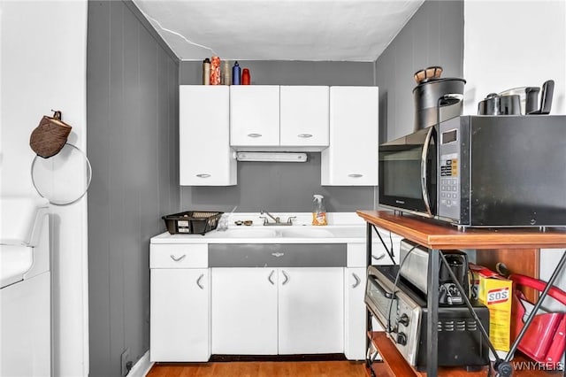 kitchen with white cabinetry, sink, wood walls, and light hardwood / wood-style flooring