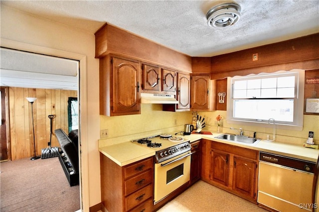 kitchen featuring stove, sink, wooden walls, a textured ceiling, and dishwashing machine