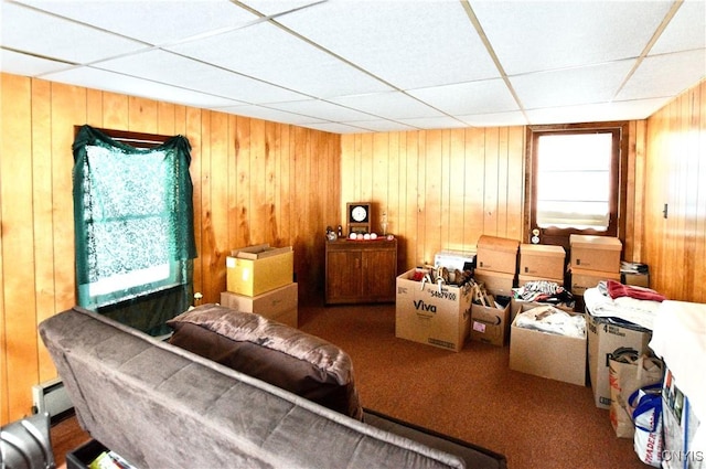 interior space with carpet flooring, baseboard heating, a drop ceiling, and wooden walls