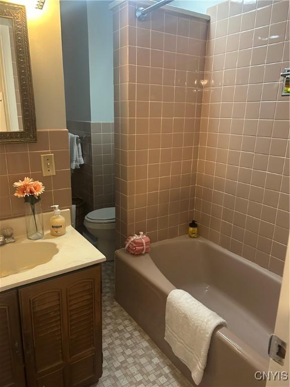 full bathroom featuring vanity, tiled shower / bath combo, tile walls, and toilet