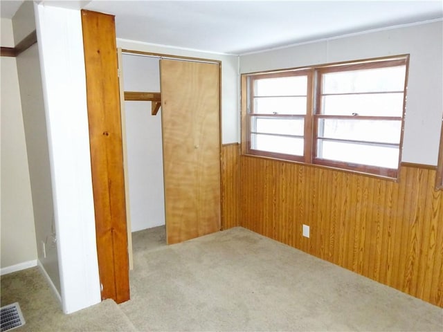 unfurnished bedroom with light carpet, wooden walls, and a closet