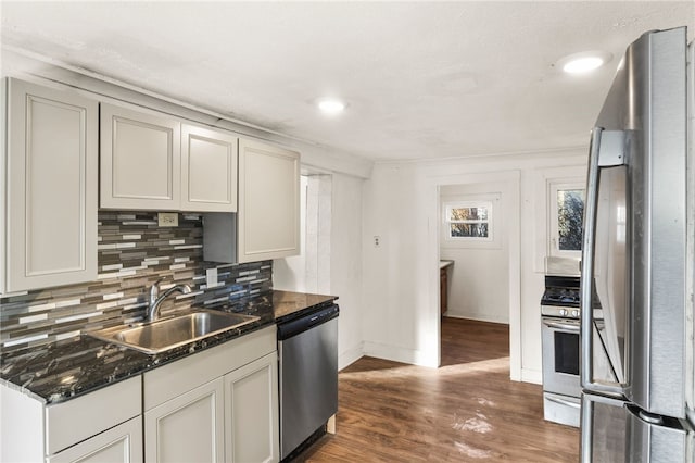 kitchen with dark wood-type flooring, sink, dark stone counters, stainless steel appliances, and backsplash