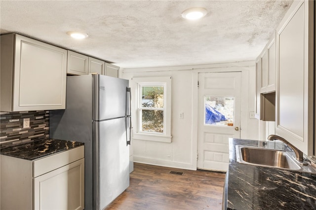 kitchen featuring dark hardwood / wood-style floors, stainless steel refrigerator, sink, dark stone countertops, and decorative backsplash