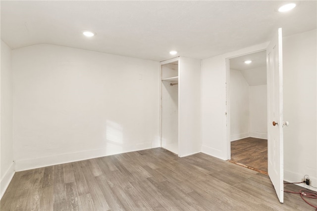 unfurnished bedroom featuring wood-type flooring, vaulted ceiling, and a closet