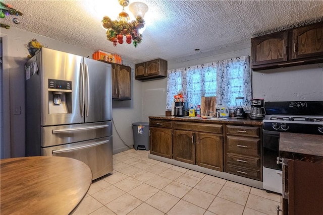 kitchen featuring a textured ceiling, dark brown cabinetry, light tile patterned floors, stainless steel fridge with ice dispenser, and white stove