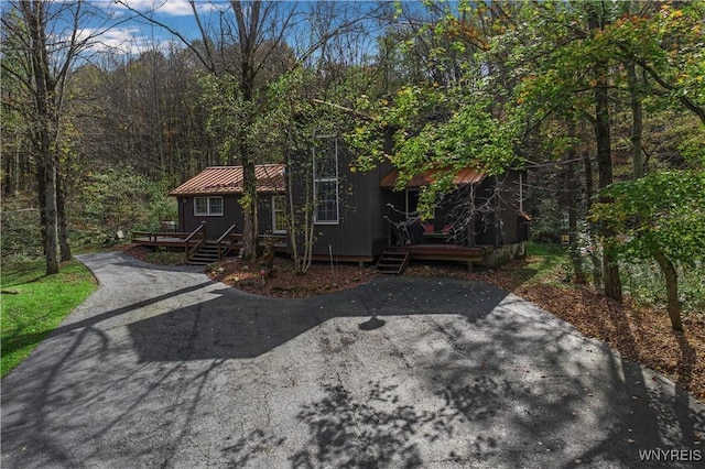 view of front of house with driveway, a view of trees, and a deck