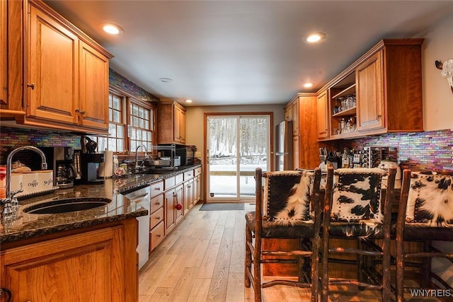 kitchen with a sink, stainless steel appliances, backsplash, and dark stone counters