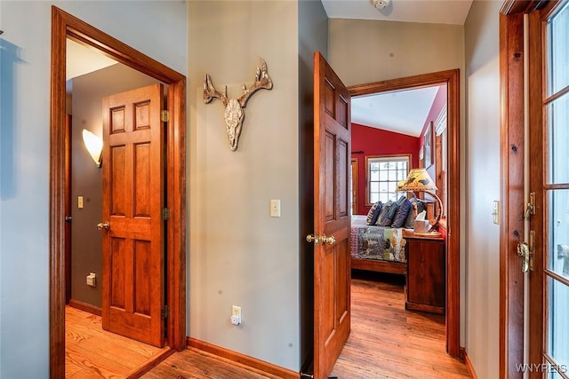 hallway featuring lofted ceiling, light wood-style floors, and baseboards