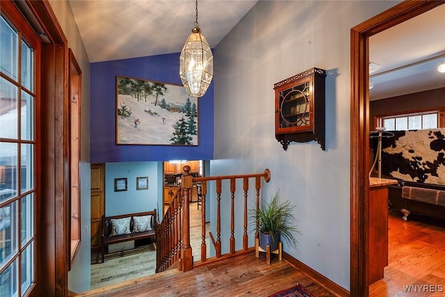 stairway featuring a chandelier, vaulted ceiling, baseboards, and wood finished floors