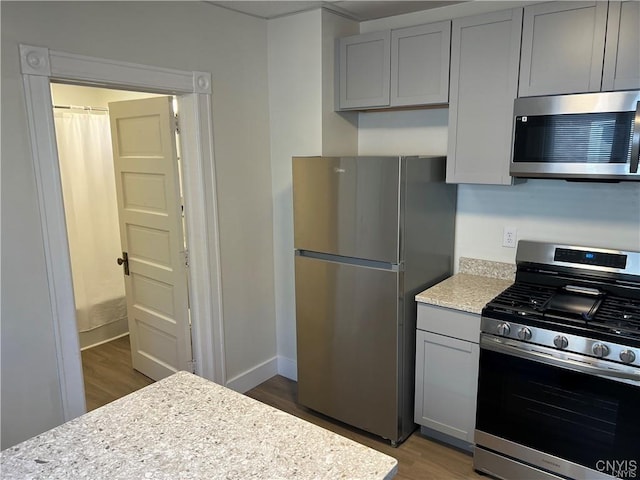 kitchen with hardwood / wood-style flooring, gray cabinets, light stone countertops, and stainless steel appliances