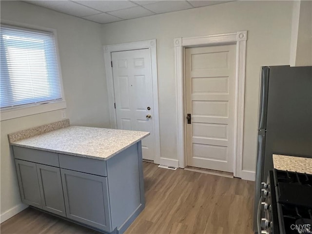 kitchen featuring a paneled ceiling, dark wood-type flooring, stainless steel fridge, range with gas stovetop, and kitchen peninsula