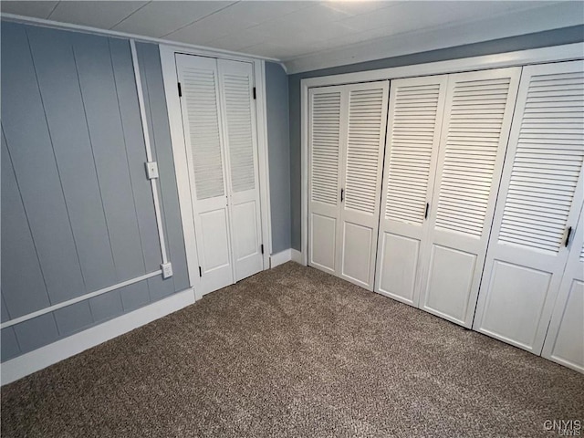 unfurnished bedroom with dark colored carpet and two closets