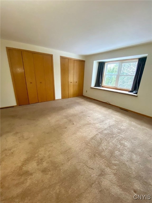 unfurnished bedroom featuring light colored carpet and multiple closets