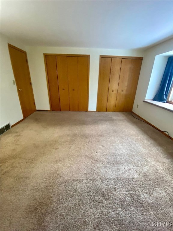 unfurnished bedroom featuring light colored carpet and multiple closets