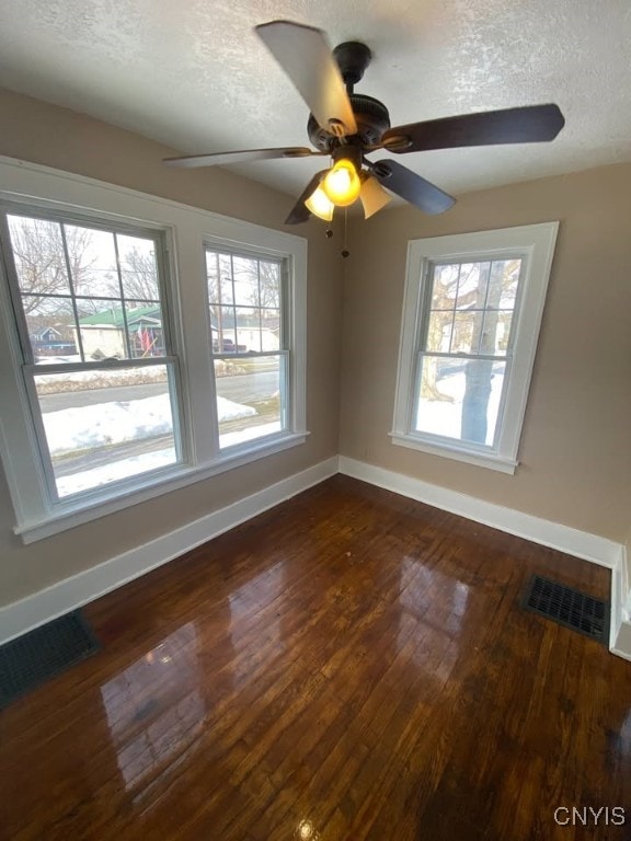 empty room with dark hardwood / wood-style flooring, plenty of natural light, and a textured ceiling