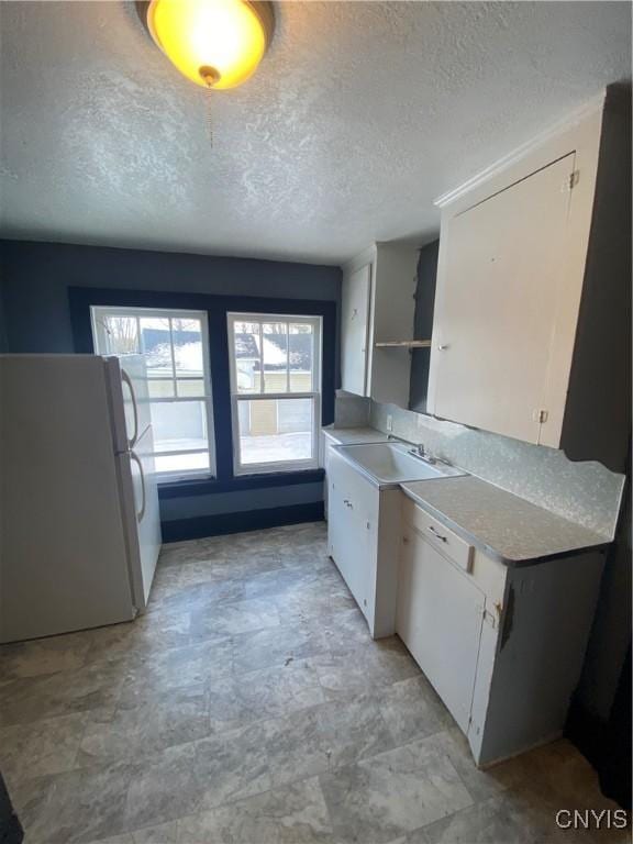 kitchen featuring white cabinets, a textured ceiling, white fridge, and sink