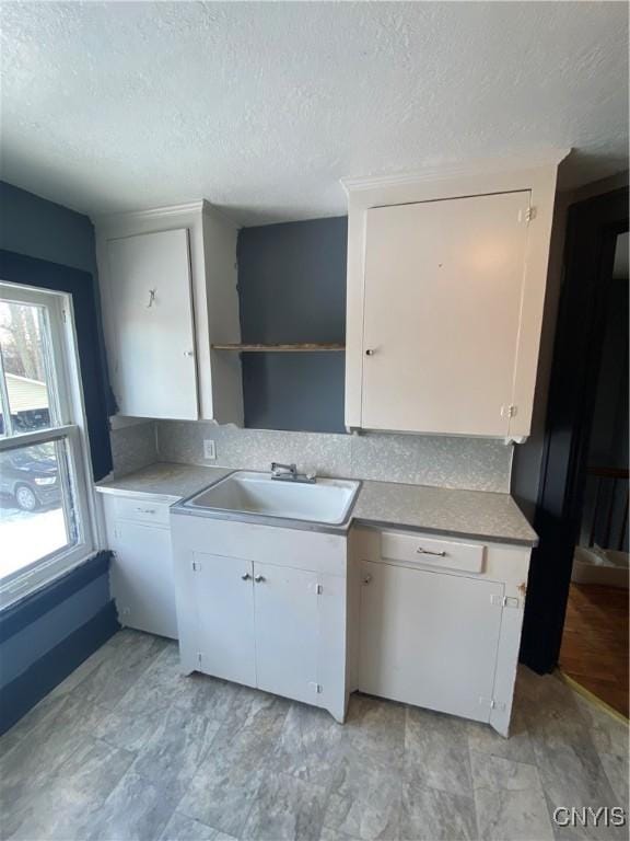 kitchen with a textured ceiling, white cabinetry, and sink