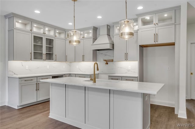 kitchen with custom exhaust hood, pendant lighting, and an island with sink