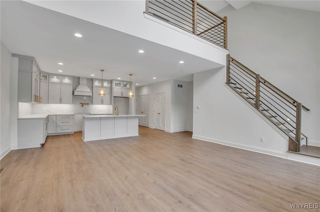 kitchen with light hardwood / wood-style flooring, pendant lighting, custom exhaust hood, backsplash, and a center island