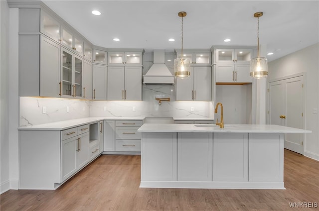 kitchen with pendant lighting, custom range hood, sink, a center island with sink, and light hardwood / wood-style floors