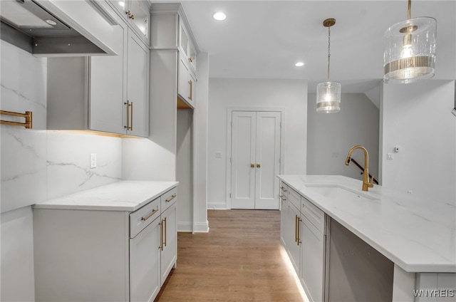 kitchen with light stone countertops, premium range hood, hanging light fixtures, decorative backsplash, and sink