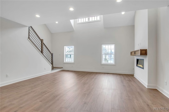 unfurnished living room with light wood-type flooring, high vaulted ceiling, and plenty of natural light