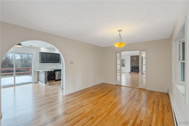 interior space with light wood-type flooring, a baseboard radiator, ceiling fan, and a large fireplace