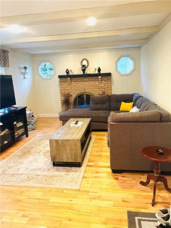 living room with beamed ceiling, light hardwood / wood-style floors, a brick fireplace, and a wealth of natural light