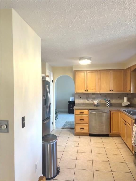 kitchen with a textured ceiling, light tile patterned flooring, stainless steel appliances, and tasteful backsplash