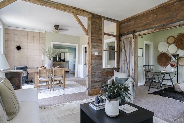 carpeted living room with a barn door, ceiling fan, and tile walls