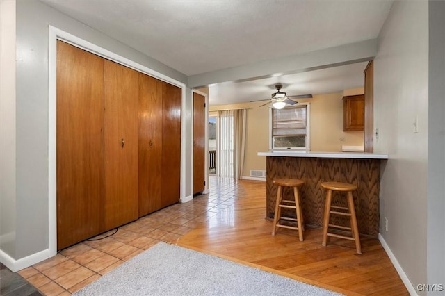 kitchen featuring kitchen peninsula, light hardwood / wood-style flooring, ceiling fan, and a breakfast bar area