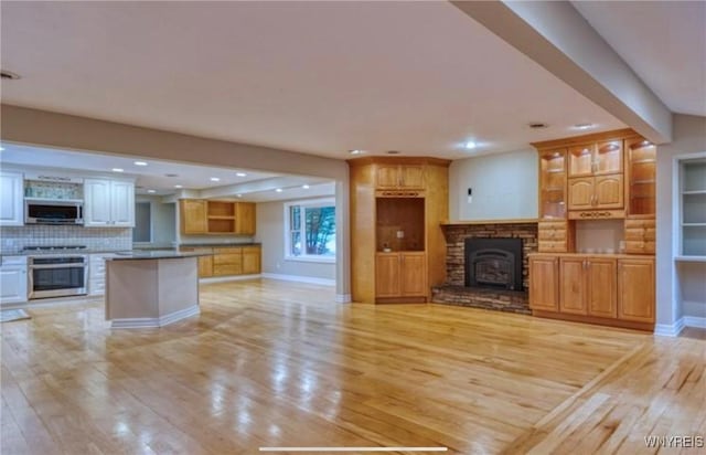 kitchen with stainless steel appliances, backsplash, light hardwood / wood-style floors, and a fireplace