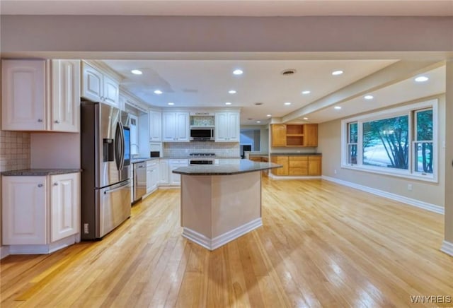 kitchen with white cabinetry, backsplash, a center island, stainless steel appliances, and light wood-type flooring