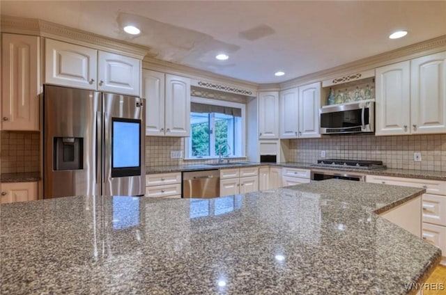 kitchen featuring appliances with stainless steel finishes, sink, white cabinets, decorative backsplash, and dark stone counters