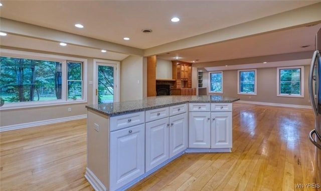 kitchen featuring stainless steel refrigerator, white cabinetry, light stone counters, light hardwood / wood-style floors, and a kitchen island