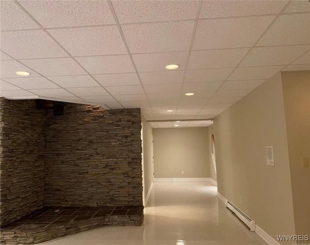 hall with a paneled ceiling and a baseboard heating unit