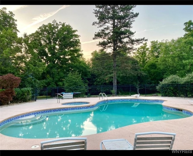 pool at dusk with an in ground hot tub, a diving board, and a patio area