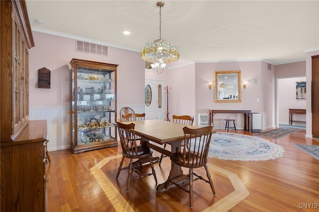 dining space featuring wood-type flooring, crown molding, and a notable chandelier