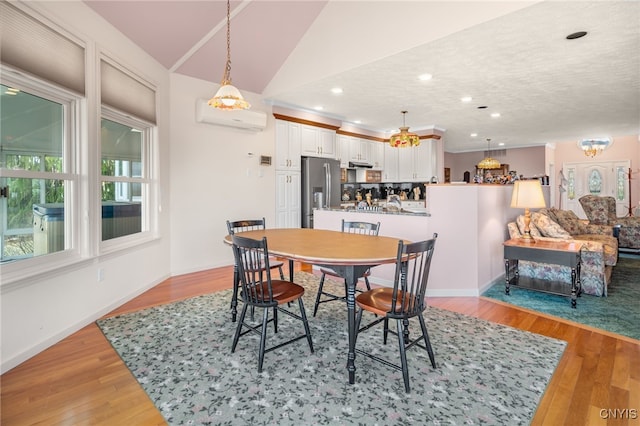 dining area with a textured ceiling, lofted ceiling, light hardwood / wood-style flooring, and a wall mounted air conditioner