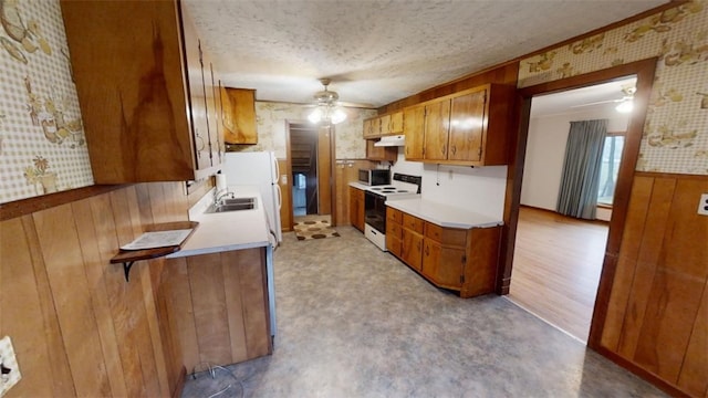 kitchen with sink, light hardwood / wood-style floors, a textured ceiling, white appliances, and wooden walls